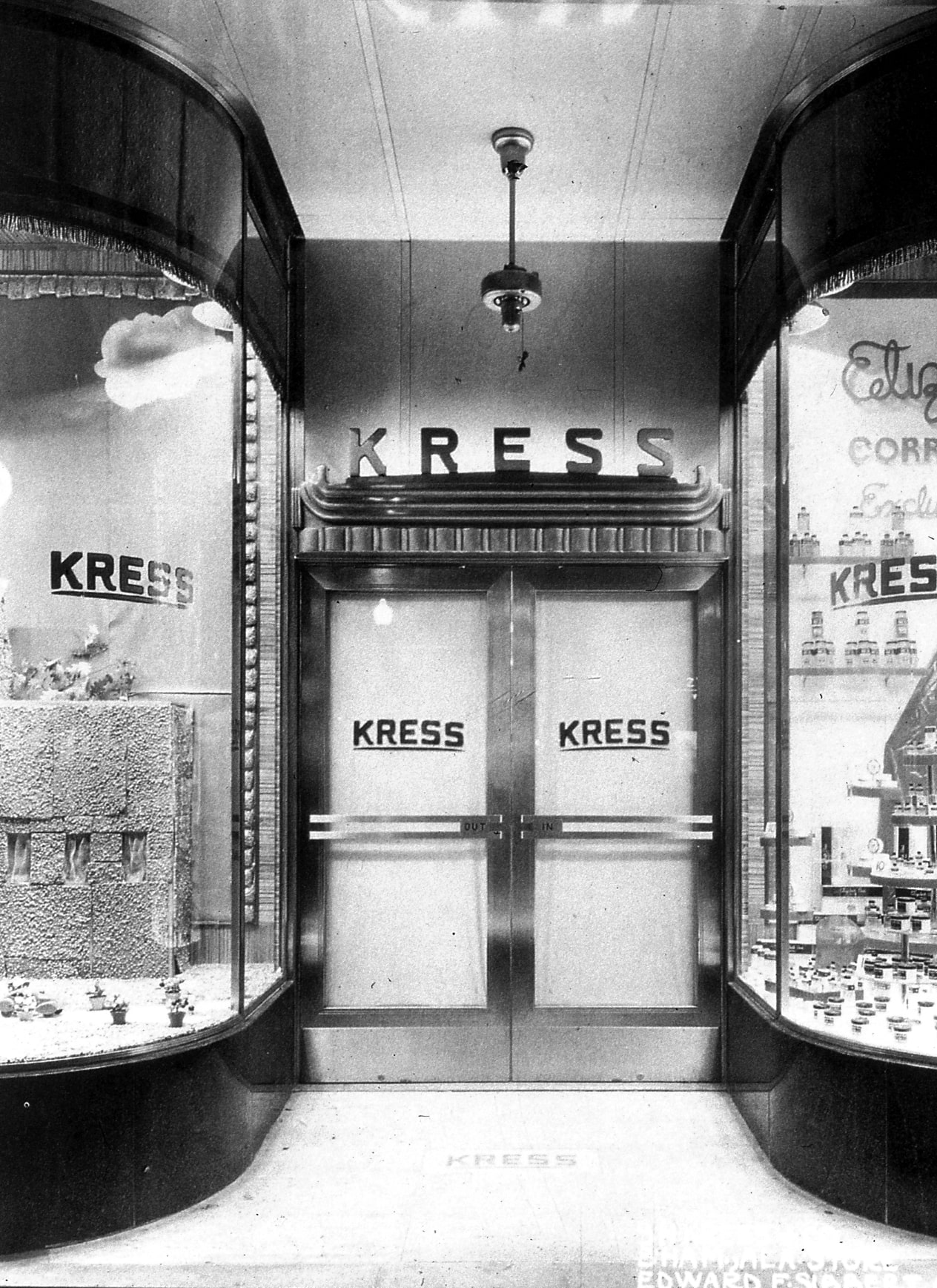 Black and white photograph of the entrance to an S.H. Kress & Company store with the curved display windows lit up.