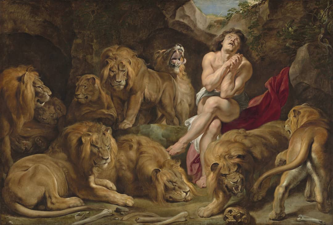 A man sits along in the midst of many lions. He claps his hands together and looks to the sky.