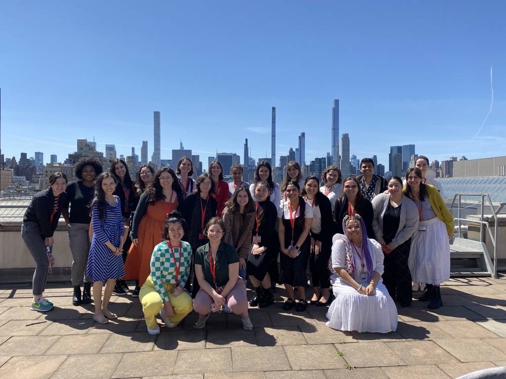 Group of individuals pose for a picture on the Met's rooftop overlooking the skyline of Midtown Manhatten